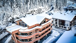 A multi-story hotel with a curved facade, large windows, and a snow-covered roof. - HAUSEREI Design & Kräuterhotel - ADULTS ONLY (Steeg)