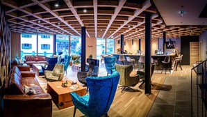 A spacious lounge area with leather sofas and patterned chairs, wooden flooring, and a bar area with stools. - HAUSEREI Design & Kräuterhotel - ADULTS ONLY (Steeg)