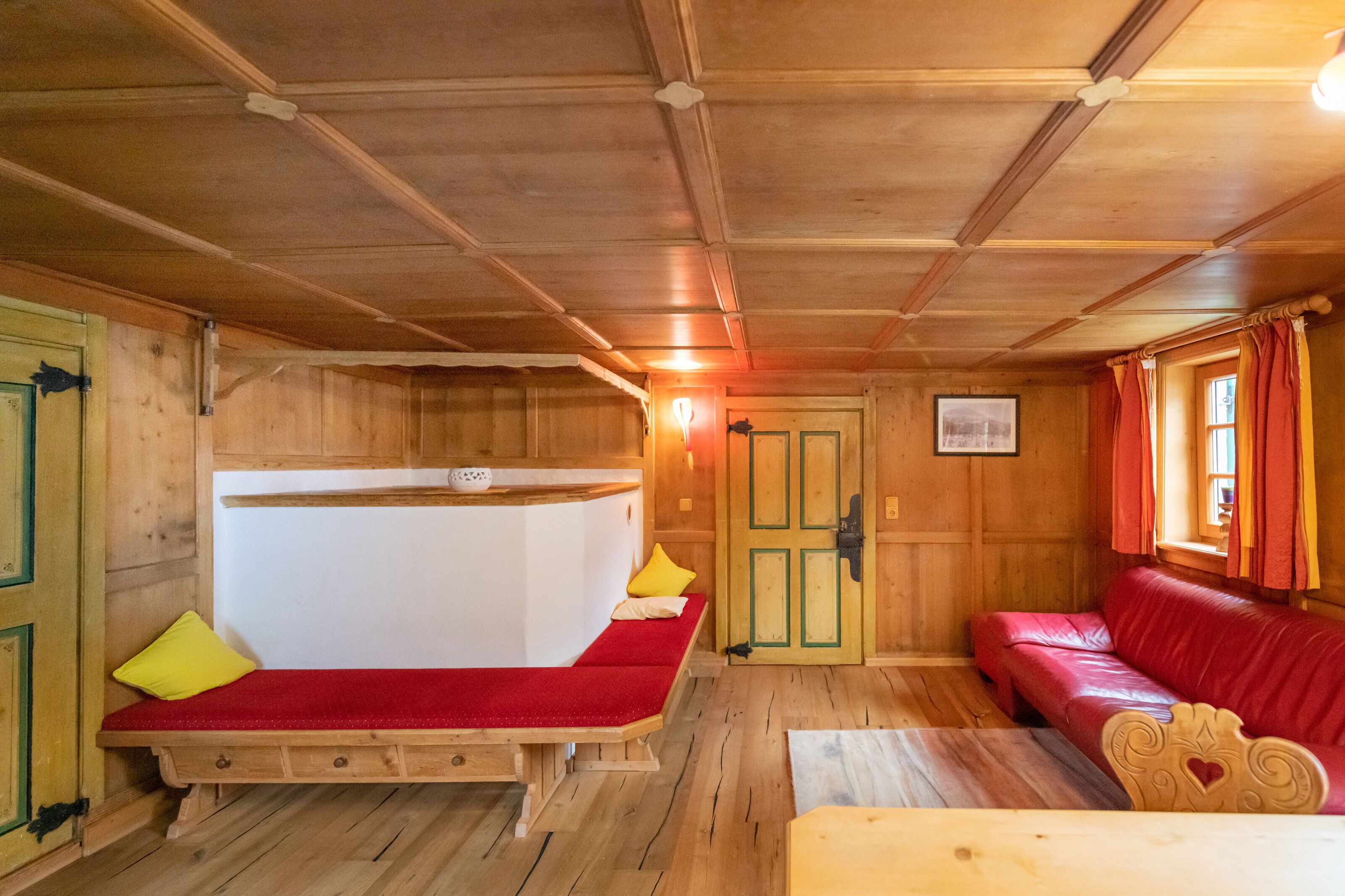 Interior de una cabaña de madera con una cama individual, un sofá rojo y una mesa de madera.