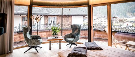 Habitación de hotel moderna con una cama grande, dos sillones, una mesita y vistas a un paisaje nevado a través de amplias ventanas.