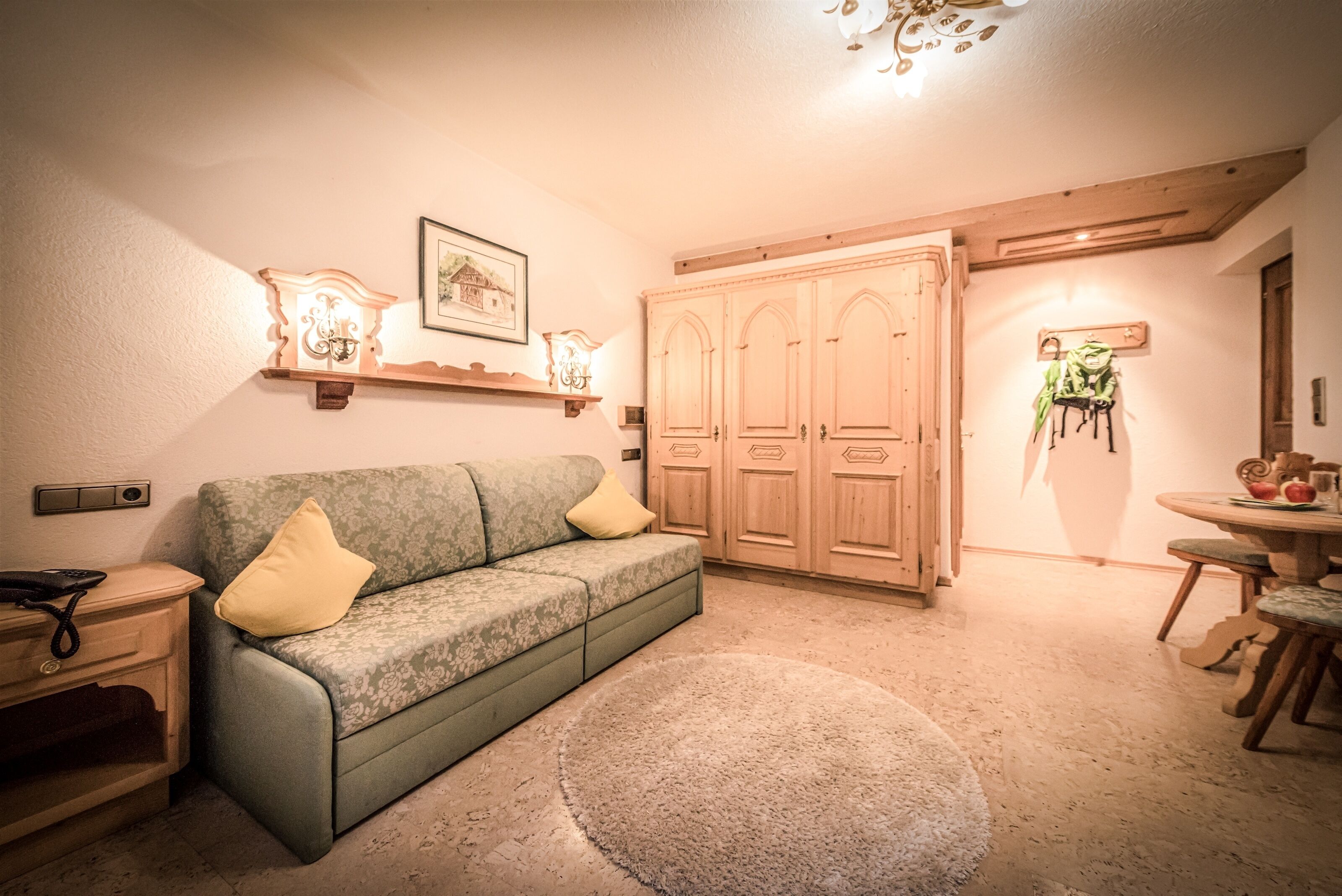 A cozy living room with a green sofa, wooden wardrobe, and a dining area with a round table and chairs.
