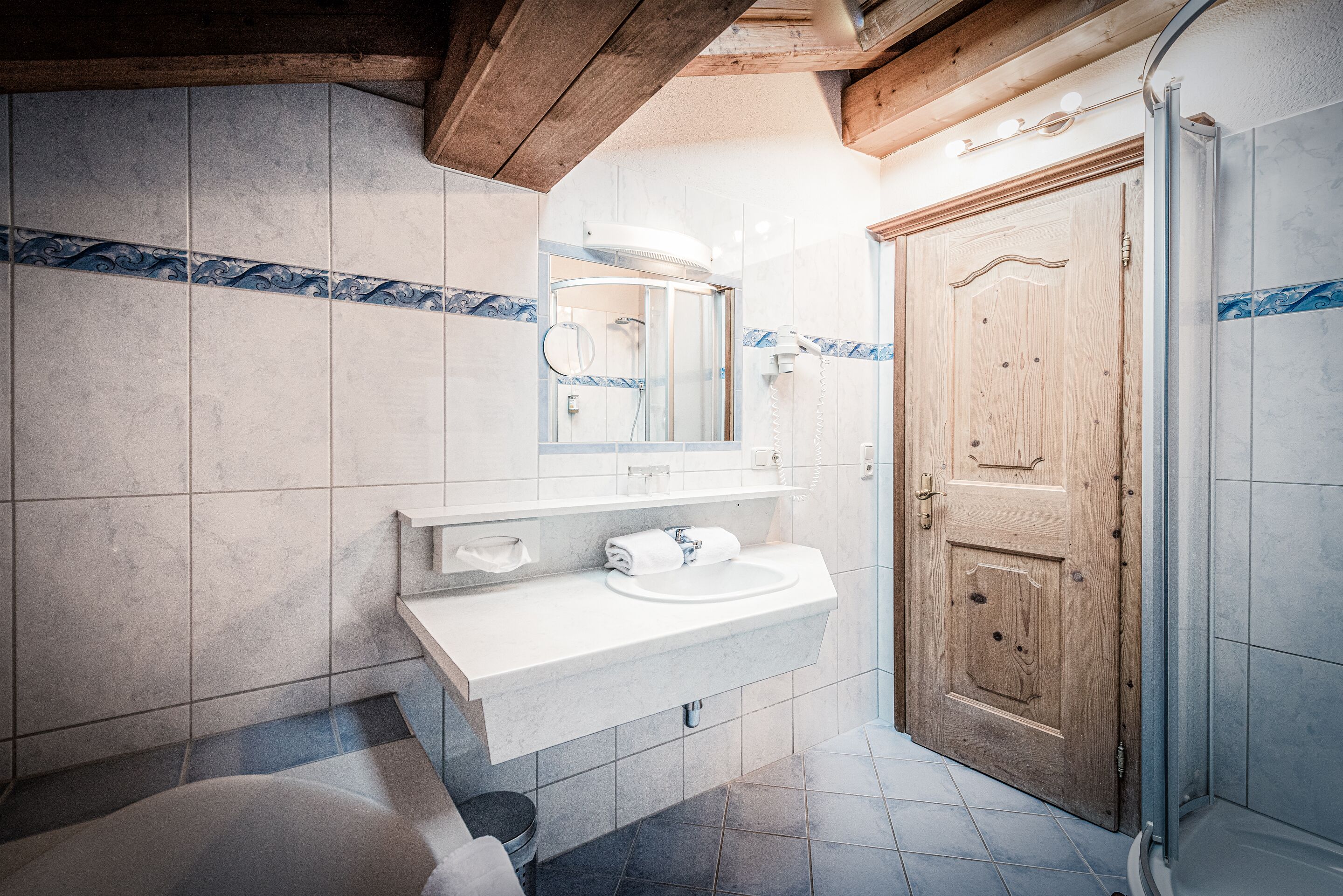Une salle de bain avec une porte en bois, un lavabo blanc et un espace douche.