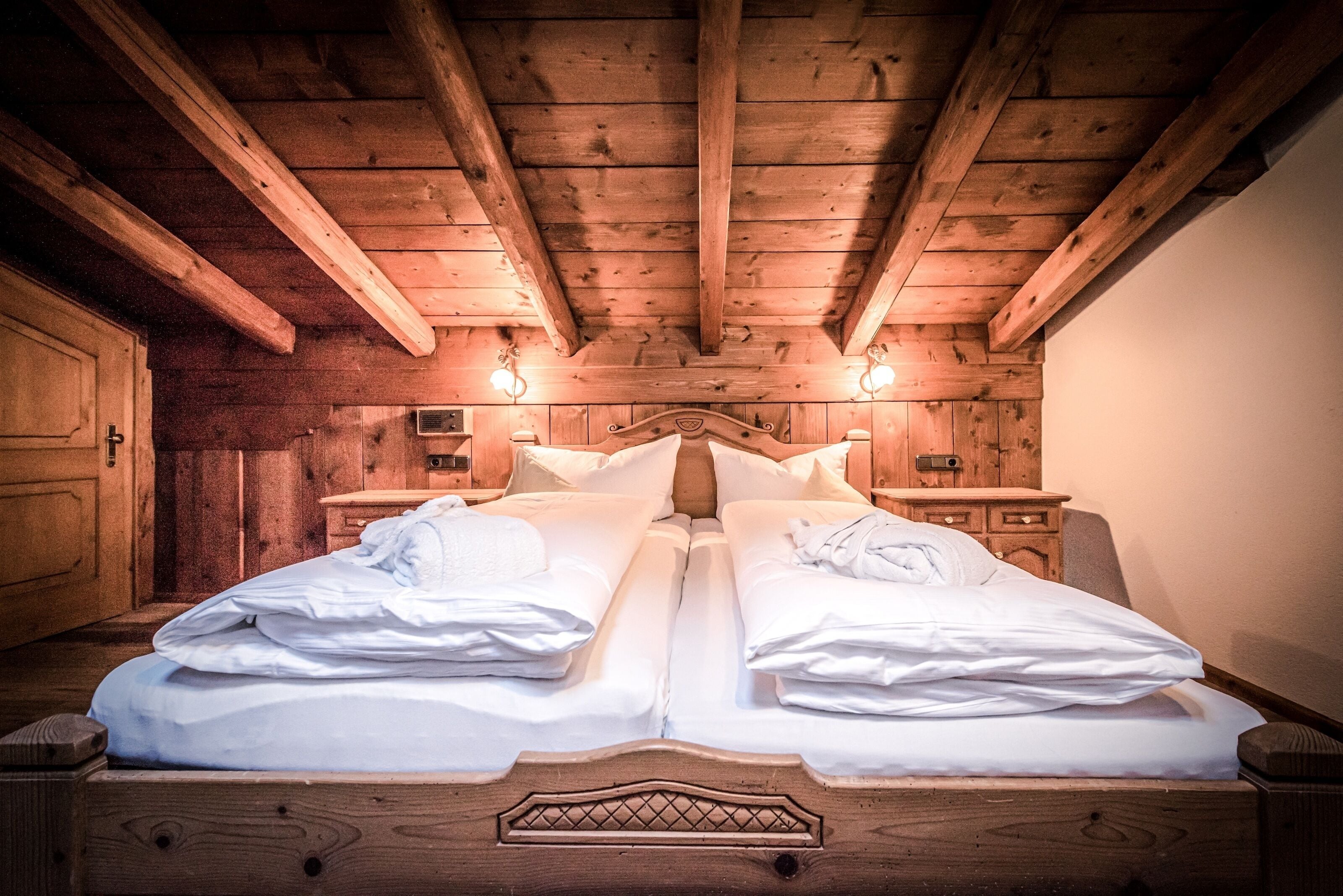A double bed with wooden headboard and nightstands, wooden ceiling beams, and wall-mounted lights.