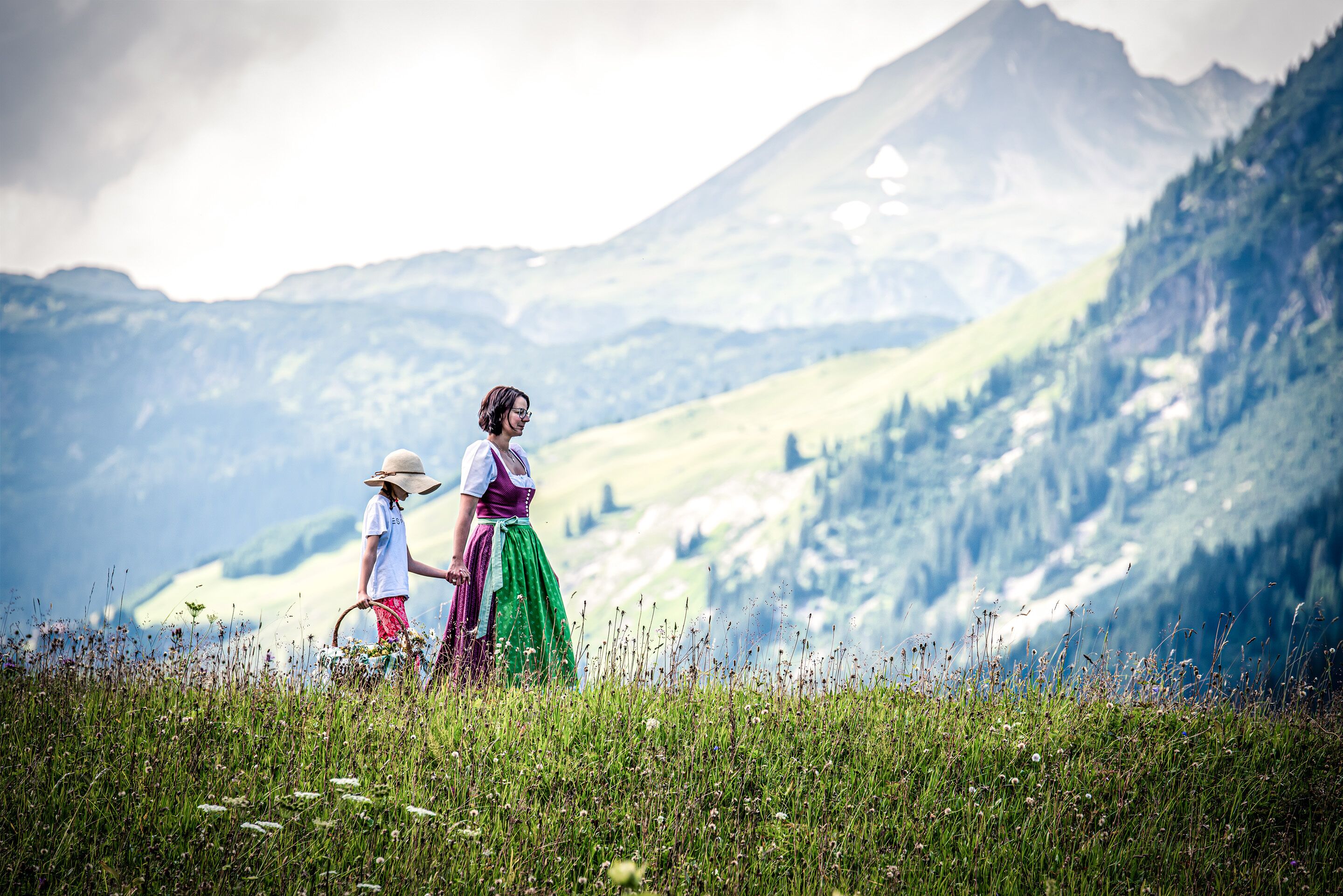 A person in traditional attire walking through a field with a mountainous backdrop.