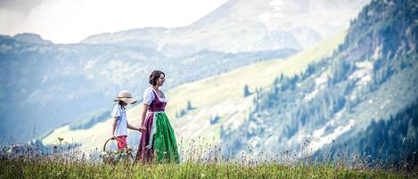 A person in traditional attire walking through a field with a mountainous backdrop.