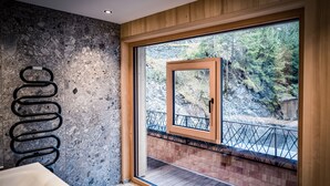 A modern bathroom with a stone wall, a wooden door leading to a balcony with a metal railing, and a white sink. - HAUSEREI Design & Kräuterhotel - ADULTS ONLY (Steeg)