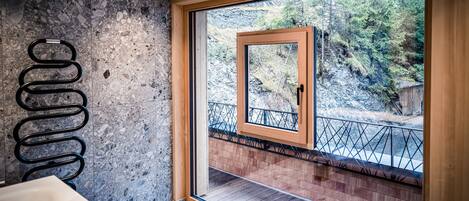 Un baño moderno con pared de piedra, una puerta de madera que da a un balcón con barandilla metálica y un lavamanos blanco.