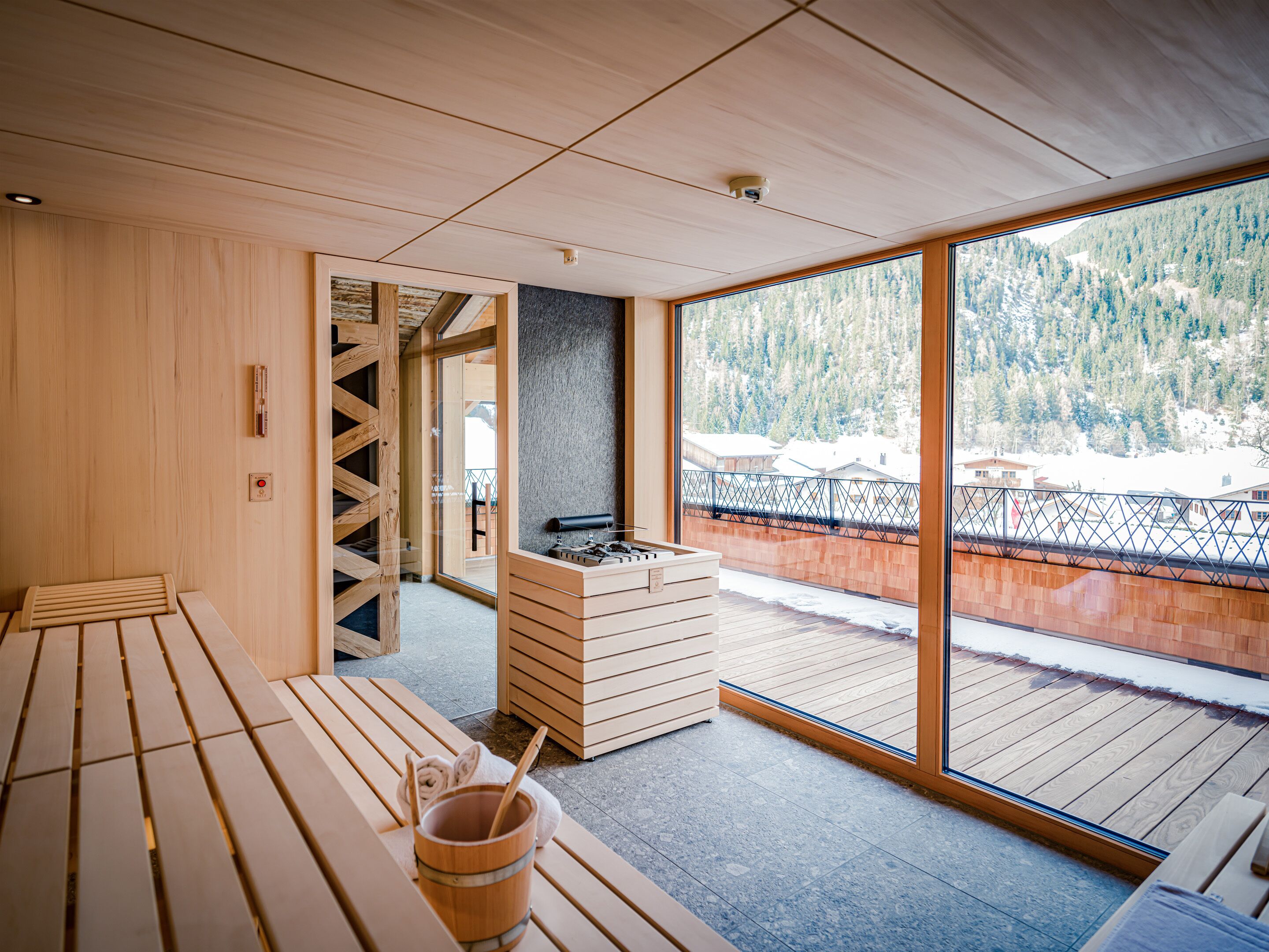 Interior de madera con sauna, un banco de madera y vistas a un paisaje nevado a través de amplios ventanales.