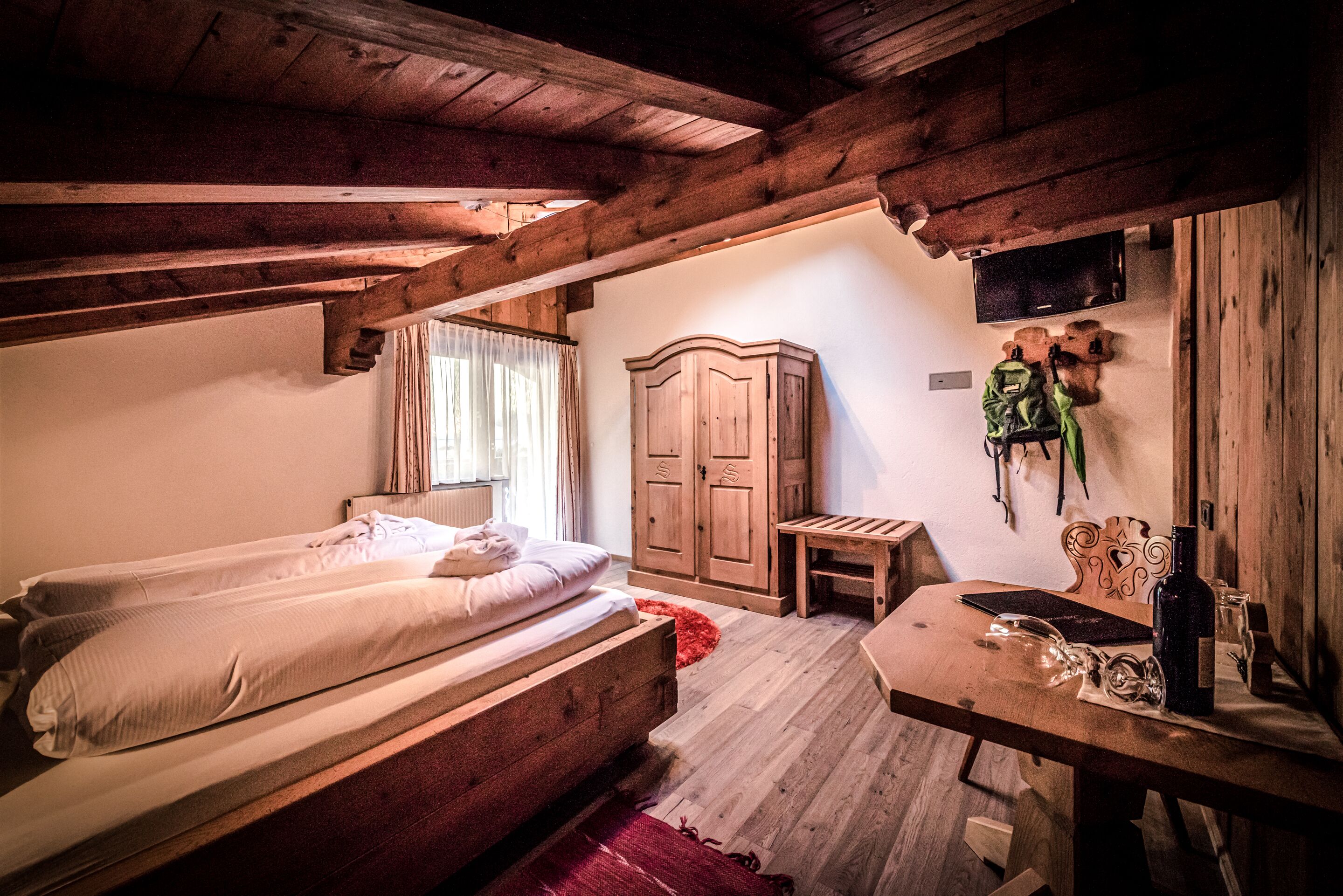 A rustic room with wooden beams, a bed, a small table, and a cabinet.