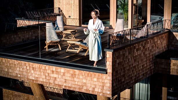 A wooden deck with lounge chairs and a person in a bathrobe. - HAUSEREI Design & Kräuterhotel - ADULTS ONLY (Steeg)