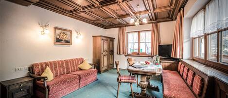 Ett traditionellt rum med ett träpanelat tak, en soffa, en bänk, ett bord och ett fönster med gardiner.