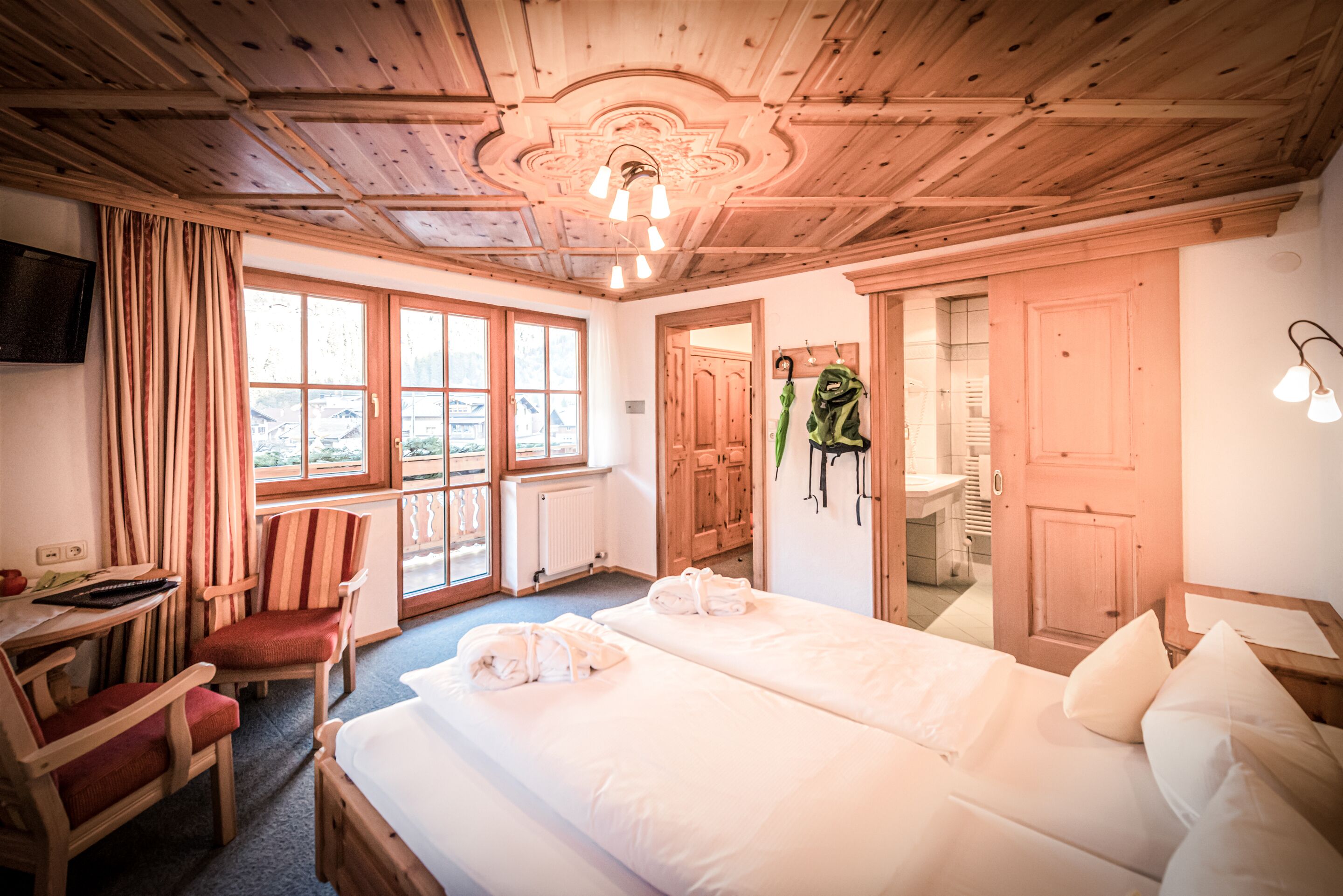A hotel room with a wooden ceiling, a bed with white linens, a desk with a keyboard, and a chair.