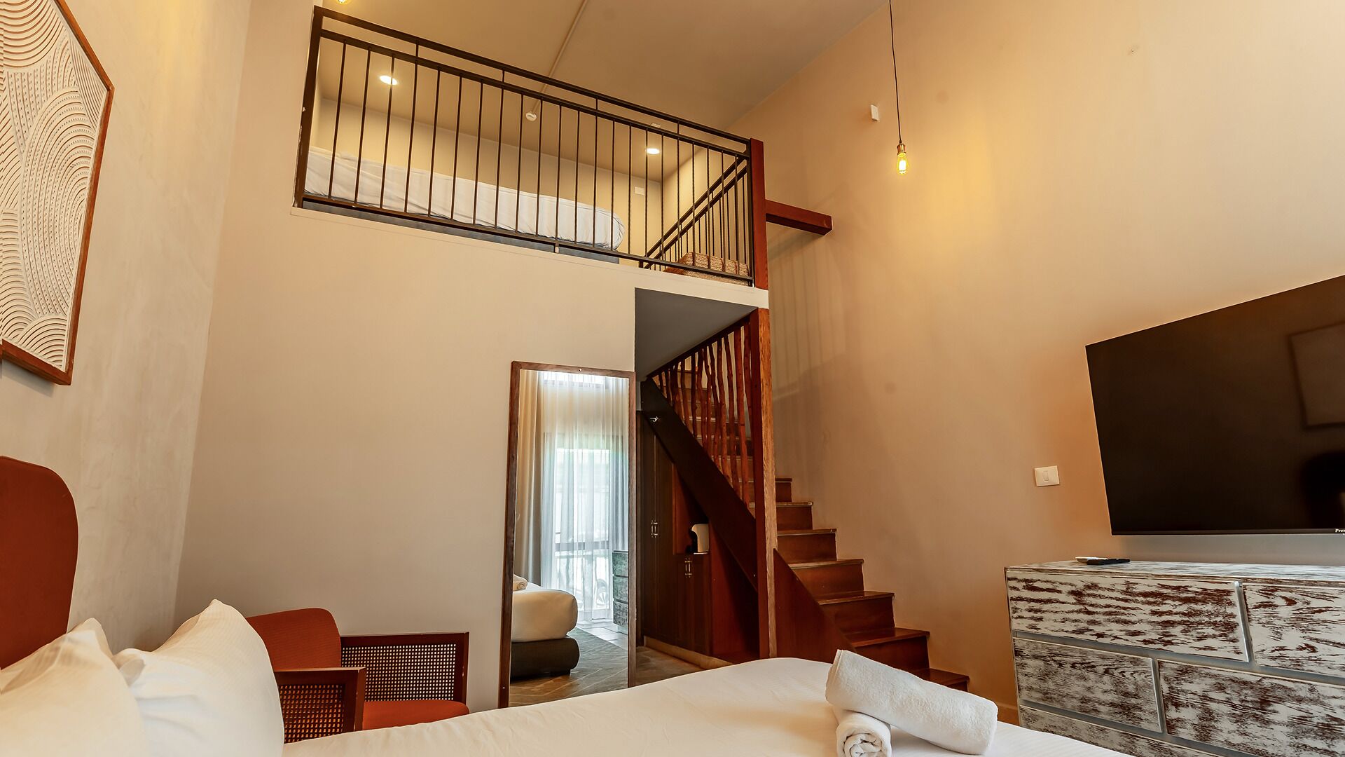 A hotel room with a bed, a chair, a staircase, and a television.