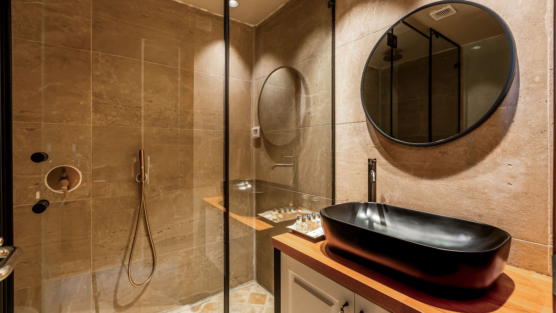 A bathroom with a glass-enclosed shower, a round mirror, and a modern sink.