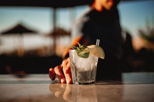 Un vaso de bebida helada con menta y una rodaja de limón sobre una superficie reflectante.