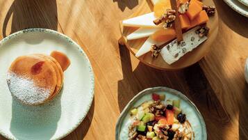 A breakfast setting with pancakes, cheese, and fruit on a wooden table.