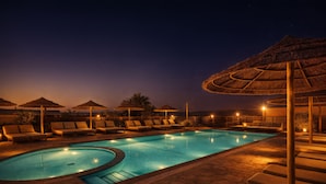 Une piscine entourée d’un sol en pierre, agrémentée de chaises longues et de parasols.