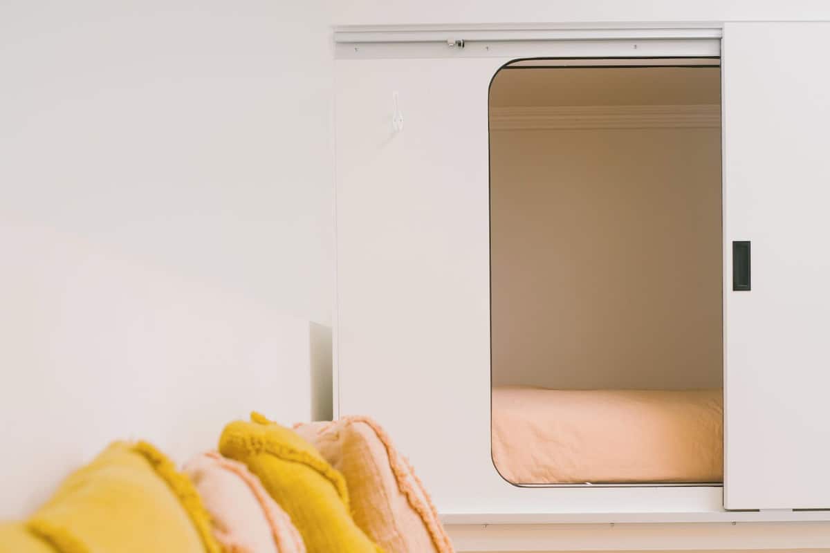 A bed with a yellow bedspread and pillows, a white wardrobe, and a white bedside table.