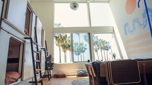 A room with bunk beds, a dining area with chairs, a large window with a view of palm trees, and a wall with abstract art.