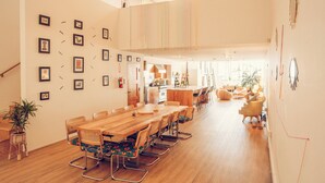 A spacious dining area with a long wooden table and chairs, a kitchen in the background, and a staircase leading to an upper level.