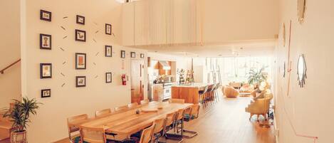 Un comedor amplio con una larga mesa de madera y sillas, una cocina al fondo y una escalera que sube a un nivel superior.