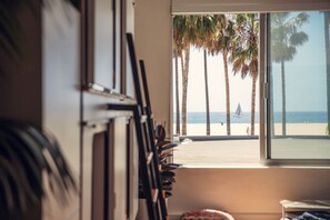 A room with a large window overlooking a beach with palm trees and a sailboat.