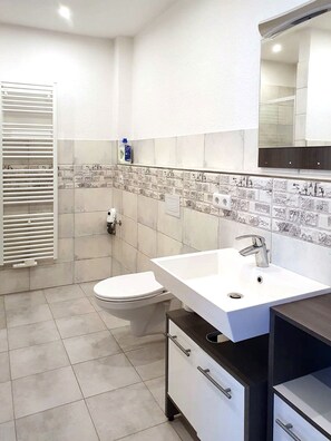 A modern bathroom with a white toilet, a white sink with a dark countertop, and a tiled backsplash. - Modern and spacious apartment, with separate access (Dohna)