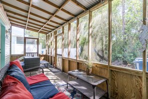 Un espace extérieur abrité, aménagé avec un banc en bois, une table et un pot de fleurs.