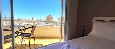 Habitación de hotel con cama, una silla y un balcón con vista a la ciudad.
