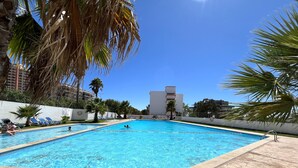 Una piscina con acqua cristallina, circondata da palme e lettini da relax.