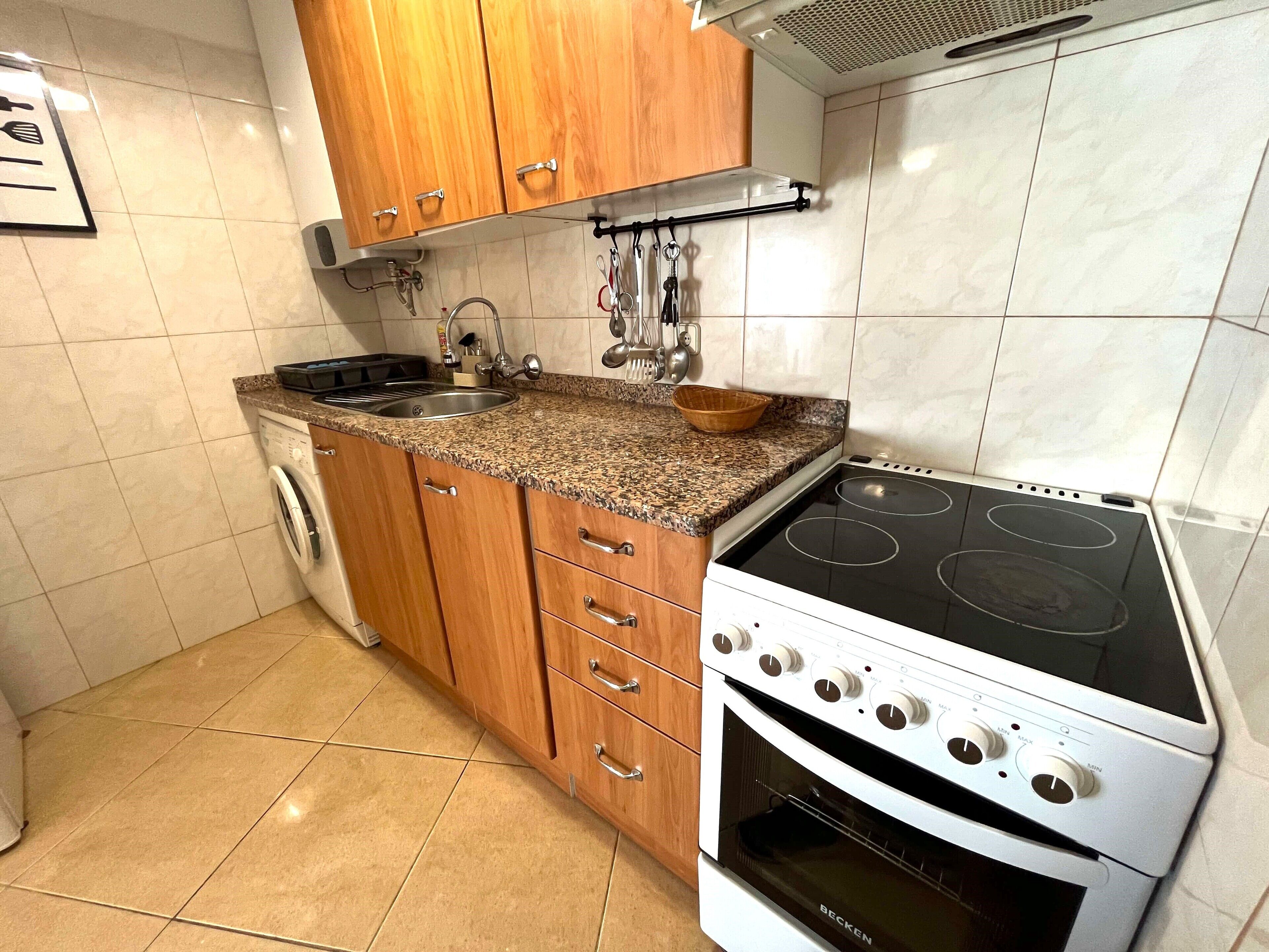 A kitchen with wooden cabinets, a granite countertop, a built-in dishwasher, a stove with four burners, and a sink.