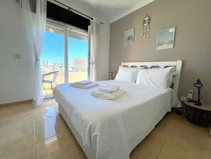 A hotel room with a large bed, a balcony with curtains, a desk with a lamp, and artwork on the wall. - Vaumar Sand Apartment (Portimão)