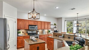 Una cocina moderna con gabinetes de madera, encimeras de granito, electrodomésticos de acero inoxidable e iluminación colgante.