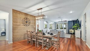 Un amplio salón con una mesa y sillas de madera para comer, una cocina moderna al fondo y un gran reloj de pared de madera.
