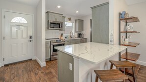 Une cuisine moderne avec des meubles blancs, un îlot central, des tabourets en bois et un four à micro-ondes encastré.