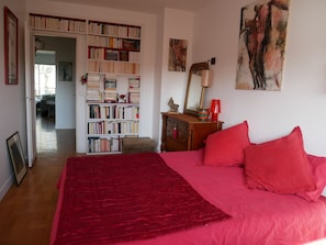 A bedroom with a large bed, a bookshelf, a desk, and a painting.