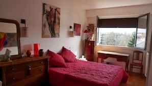 Ein Schlafzimmer mit Bett, Kommode, Schreibtisch, Stuhl und einem großen Fenster.