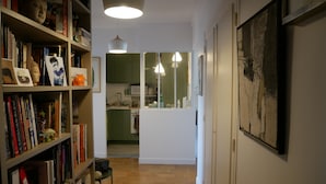 Ein Flur mit Bücherregalen, einem Essbereich und einer durch eine geöffnete Tür einsehbarer Küche.