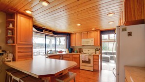 A kitchen with wooden cabinets, a large island with stools, a microwave, and an oven. - The Swedish Fish: Getaway on Lake Saint Clair! (Olympia)