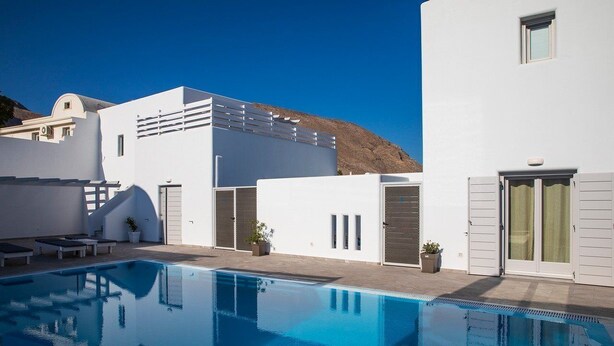Un edificio moderno blanco con piscina, un área de patio con sillones de descanso y una montaña al fondo.