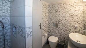 Un baño con baldosas de diseño geométrico, inodoro, lavabo y zona de ducha.