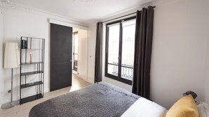 A hotel room with a bed, a bedside table, a lamp, a bookshelf, and a window with curtains. - Jehan, 2BR/1BA, 4 people (París)