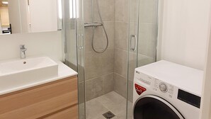 A modern bathroom with a glass-enclosed shower, a sink, and a washing machine. - Charles V, 2BD/ 2BA, 6 people (París)