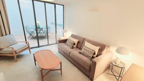 A modern living room with a sofa, a wooden coffee table, a chair, and a glass dining table with chairs outside a sliding glass door. - Charles V, 2BD/ 2BA, 6 people (París)