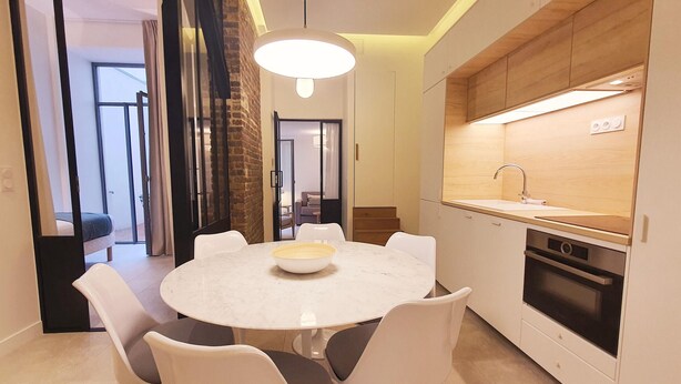 A modern kitchen with white cabinetry, a built-in oven, and a round dining table with white chairs. - Charles V, 2BD/ 2BA, 6 people (París)