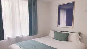 A neatly arranged bedroom with a large bed, a ceiling light, a window with curtains, and a framed picture on the wall. - Charles V, 2BD/ 2BA, 6 people (París)