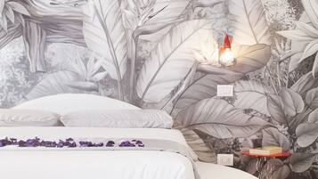 Une chambre avec un lit blanc, une table de chevet surmontée d’une lampe rouge et une fresque murale représentant des feuilles tropicales.