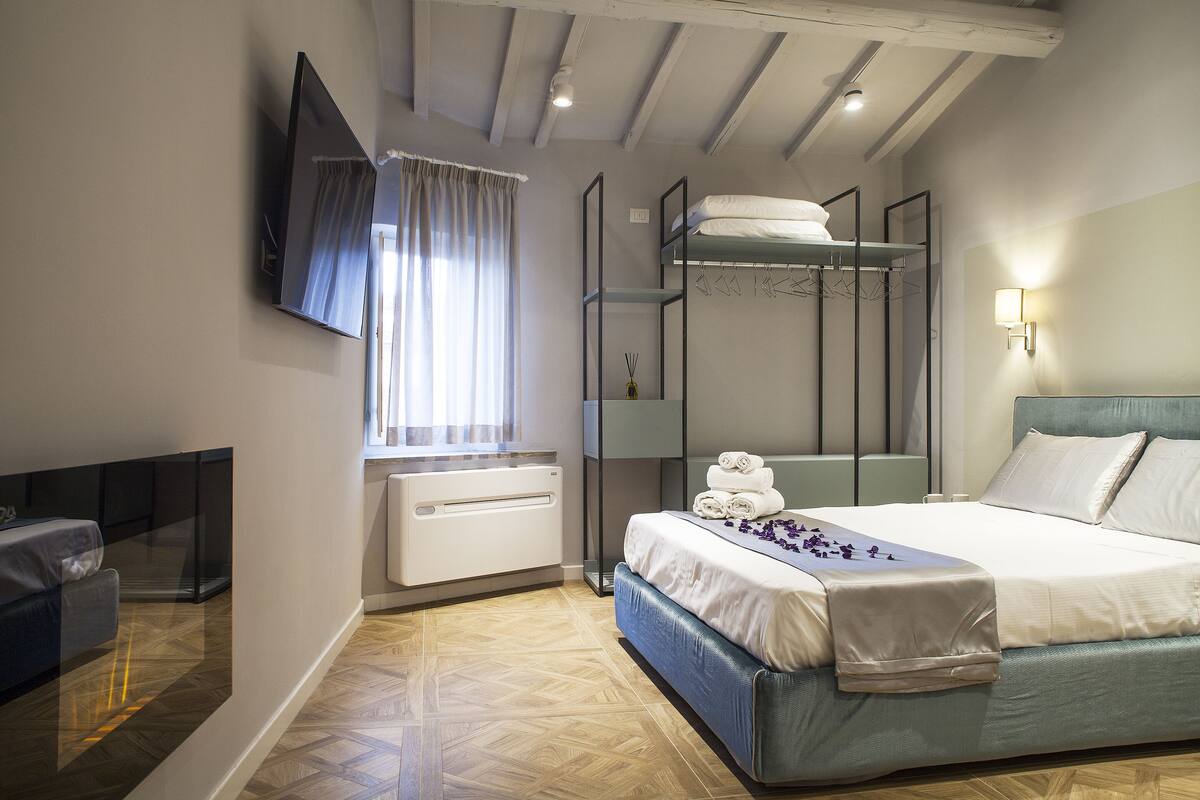 A bedroom with a bunk bed, a flat-screen TV mounted on the wall, a bedside table, and a window with curtains.