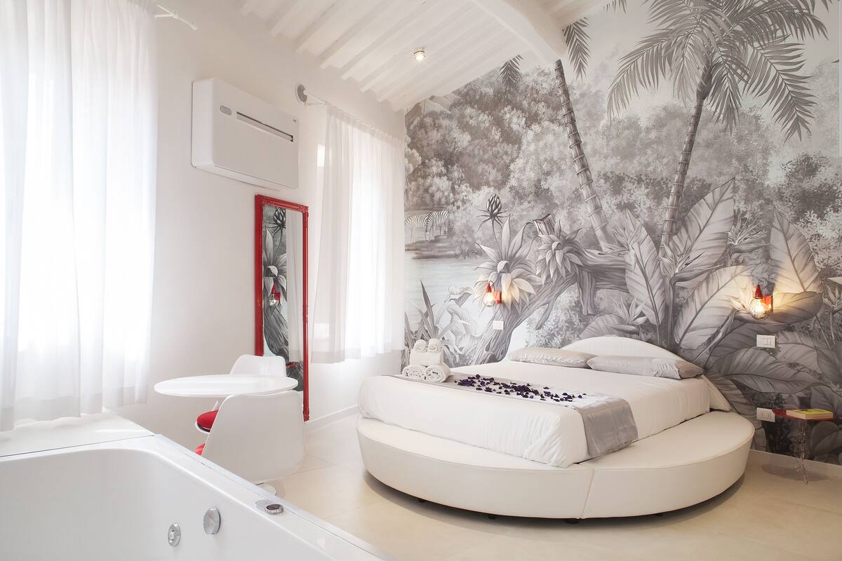 A modern bathroom with a bathtub, a round bed, and a wall mural.