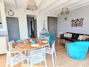 Un soggiorno moderno con un tavolo da pranzo in legno, sedie bianche, una poltrona blu, un divano nero e un’opera d’arte a parete.